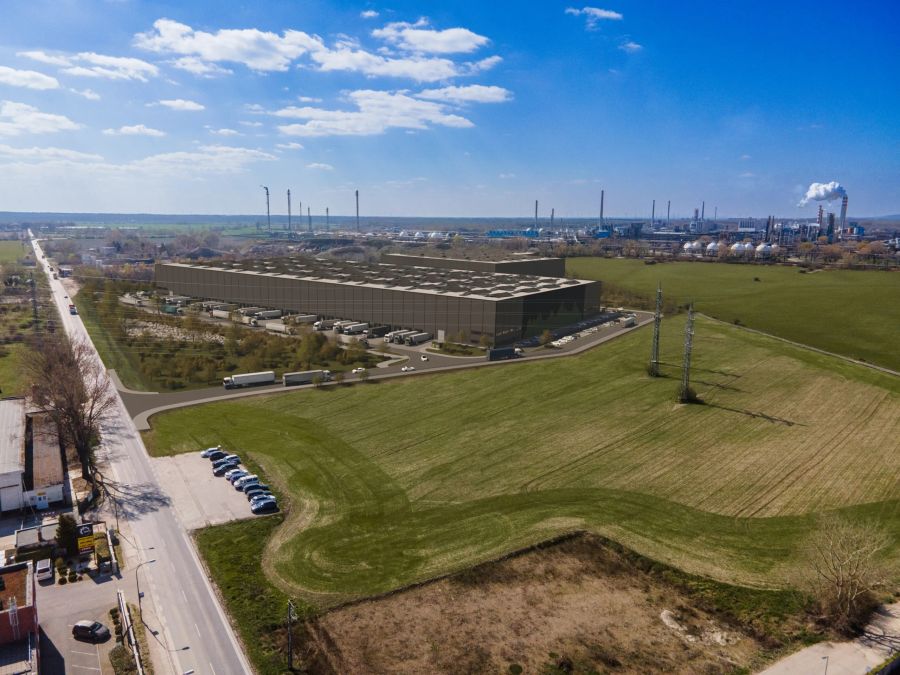 Letecký pohľad na veľkú modernú logistickú halu obklopenú zelenými poliami a cestami s nákladnými autami. V pozadí je priemyselná zóna.