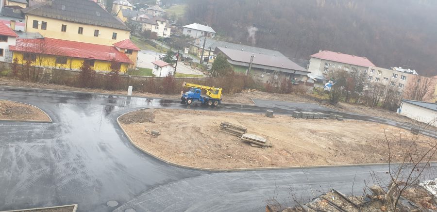 Stavebný pozemok s novými asfaltovými cestami, nespevnenými plochami a mobilným žeriavom, situovaný pri zástavbe obce.